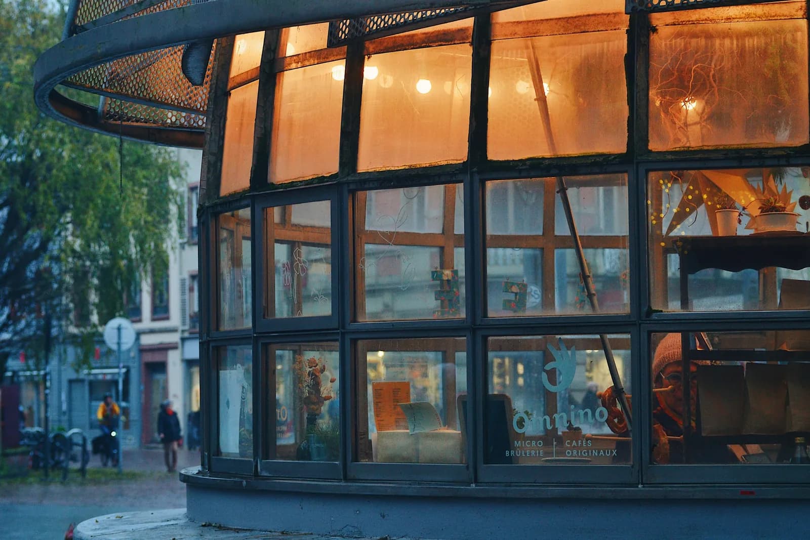 A glass kiosk glowing with warm interior light at dusk.